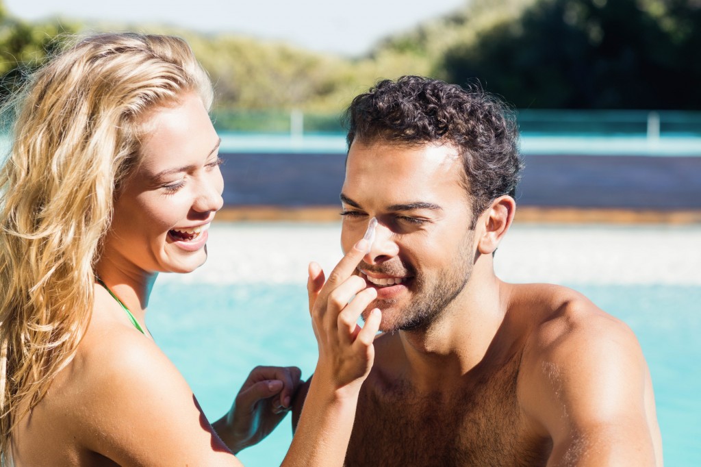 Girlfriend applying cream to boyfriend at the pool